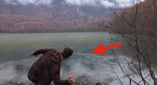 man skips rock on frozen lake